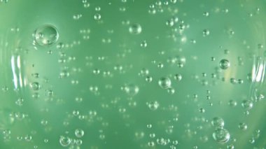 Meyve suyu aloe vera 'sının hareketi. Yeşil sıvı krem, yüzeyde kozmetik jel sıvısı dönüşü. Baloncuklu güzellik ürünü örneği. Üst Manzara. Yavaş çekim.