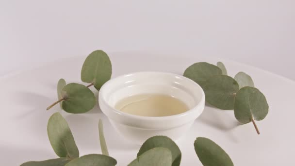 Aceite de eucalipto con hojas sobre fondo blanco. Extracto de eucalipto, aceite esencial aromático. Cosméticos naturales para el cuidado del cabello y la piel. — Vídeos de Stock