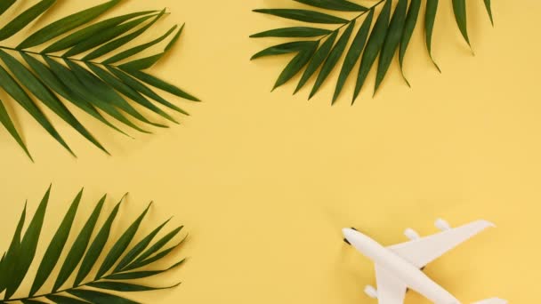 Modèle d'un avion jouet de couleur blanche et feuilles de palmier sur un fond jaune. Les avions de passagers volent, bougent. Concept de transport aérien, tourisme, vacances, voyage. Vue du dessus — Video