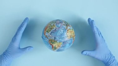 Doktorlar ellerinde tıbbi eldiven tutarak Dünya 'yı bir ellerle koruyorlar. Dünya Salgın Tehlikesi. Çevre koruma, gezegeni kurtarma, barış ve virüs kavramını koruma