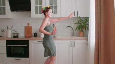 Aktif genç bir kadın dans ediyor, uzaktan kumandaya şarkı söylüyor, müzik videoları izliyor, modern bir mutfakta müzik dinliyor, evde yemek hazırlıyor, kendi başının çaresine bakıyor.