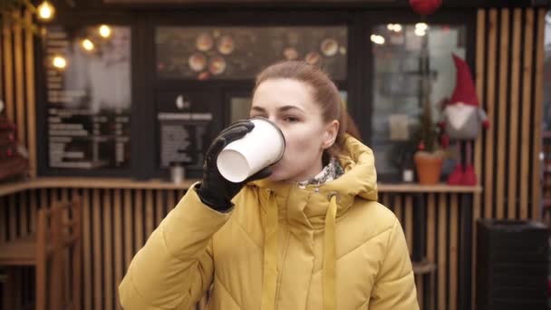 Potret wanita muda minum kopi. Gadis dewasa yang cantik berdiri di jalanan kota dengan cangkir kertas minuman panas. — Stok Video