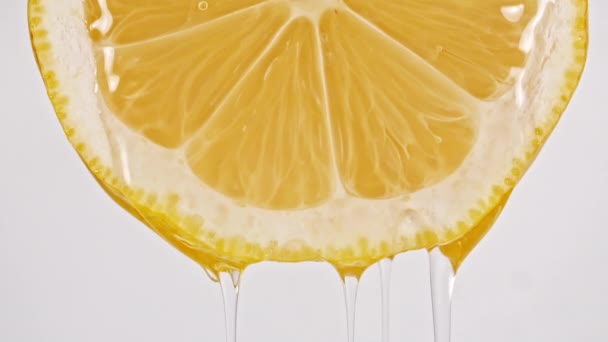 Mouvement lent de l'écoulement du jus de tranche de citron sur fond blanc. Macro Shot. — Video