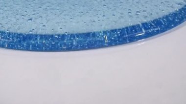 Beyaz yüzeyinde molekül kabarcıkları akan mavi şeffaf kozmetik jel kremi. Makro Vuruş