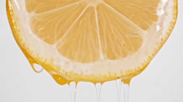 Makroaufnahme des Fließens von Saft und Ölstrom aus Zitronenscheibe auf weißem Hintergrund. Zeitlupe — Stockvideo