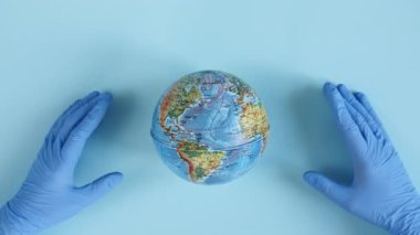 Doktorlar ellerinde tıbbi eldiven tutarak Dünya 'yı bir ellerle koruyorlar. Dünya Salgın Tehlikesi. Çevre koruma, gezegeni kurtarma, barış ve virüs kavramını koruma