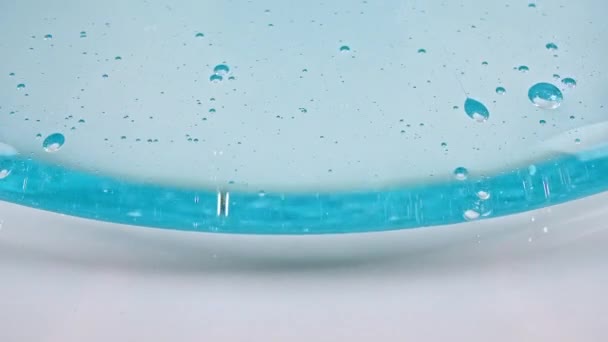 Fluide cosmétique transparent bleu avec bulles coulant sur une surface blanche. Macro Shot — Video