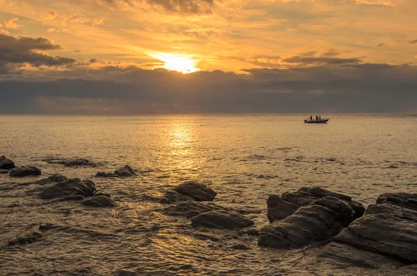 Drammatico tramonto sull'oceano con rocce di masso e barca da pesca — Foto Stock