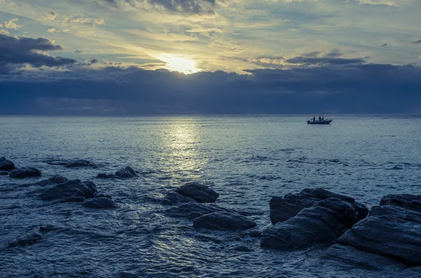 Drammatico tramonto sull'oceano con rocce di masso e barca da pesca — Foto Stock