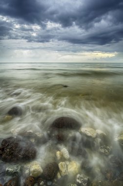 dramatik kara bulutlar ile sahilde rock isabet dalga