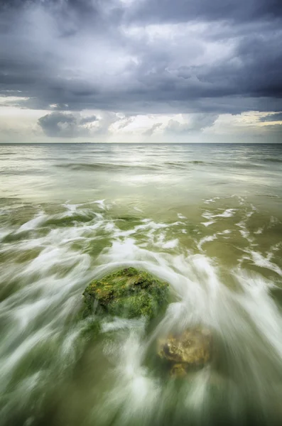 Flusso di onde morbide sopra la roccia e muschioso colpire lo sfondo shore.dramatic nuvole scure prima della tempesta — Foto Stock