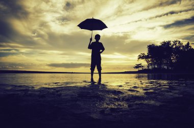 siluet duran bir çocuk kavramı görüntü ve güzel gündoğumu günbatımı arka plan ile plajda bir şemsiyeyi tut