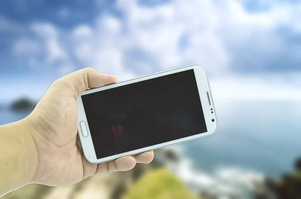 Концептуальне зображення обрізана рука тримає мобільний телефон над розмитим фоном природи — стокове фото