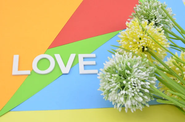 Три обрезанных искусственно зеленый и желтый цветок на цветном фоне с белым словом любовь из дерева — стоковое фото
