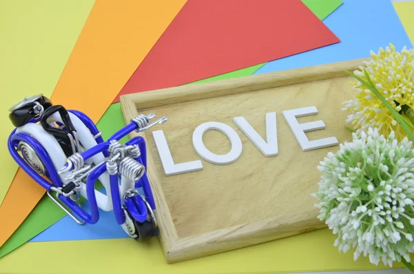 Белое слово и черный символ любви на заднем плане: зеленый, желтый и белый искусственный цветок. мини-синий скутер, расположенный слева — стоковое фото