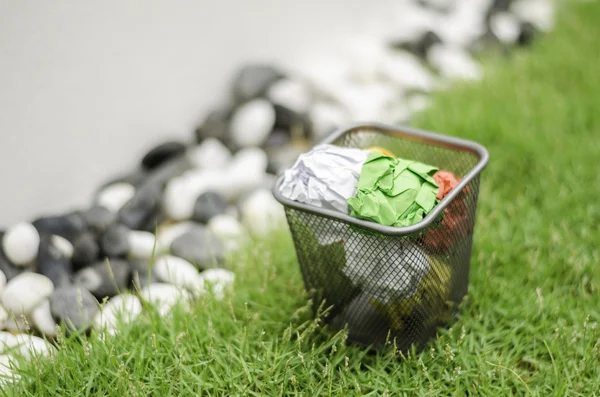 Colourful waste paper on garbage can. surrounding by green grass — Stock Photo, Image