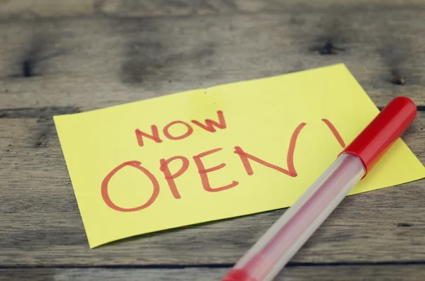 Hand writing sign, "now open" written on yellow sticky paper. dark wooden background — Stock Photo, Image