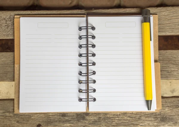 Vista superior do caderno em branco com caneta amarela ao lado na mesa de madeira — Fotografia de Stock