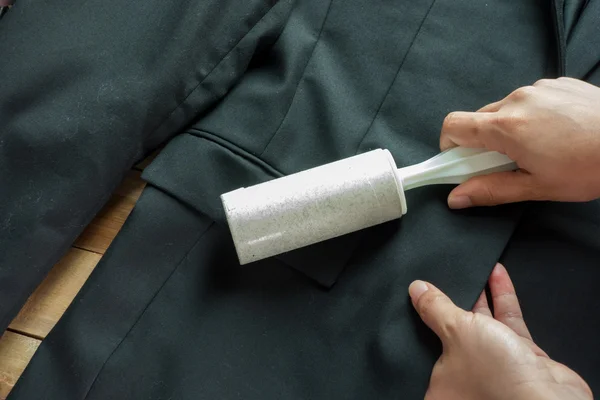 Limpeza a seco e tema de negócios: uma mão de homem com terno preto segurando uma escova pegajosa branca para limpar roupas e móveis de poeira — Fotografia de Stock