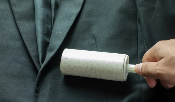 Nettoyage à sec et thème d'affaires : une main d'homme avec costume noir tenant une brosse blanche collante pour nettoyer les vêtements et les meubles de la poussière — Photo