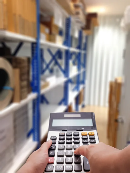 Le concept de coût d'entrepôt par calculatrice et fond d'étagère flou — Photo