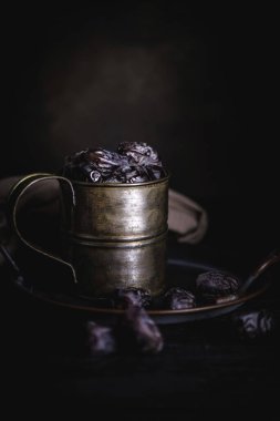 Siyah bir kupa ve tabakta birkaç hurma siyah bir arka planda siyah bir masanın üzerinde yatar. Kırsal biçim.