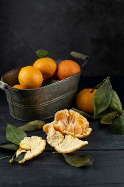 Konteynırda yaprakları olan birkaç mandalina siyah bir masanın üzerinde koyu bir zemin üzerinde yatıyor. Rustik biçim kopyalama uzayı.