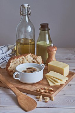 Beyaz bir masada peynirli kremalı püre çorbasının yakın çekimi. İçindekiler: mantar, soğan, kraker, ekmek, peynir, süt ve tereyağı. Kırsal biçim.