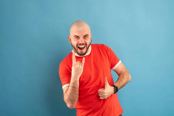 Ein Mann mittleren Alters mit Bart steht in einem roten T-Shirt vor blauem Hintergrund mit ausgestreckten Armen und jubelt über den Sieg. Isoliert. — Stockfoto