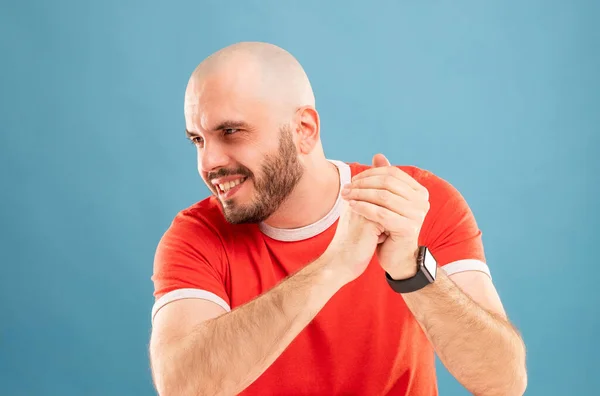 Ein bärtiger Mann mittleren Alters in rotem T-Shirt auf blauem Grund schaut glücklich zur Seite. Seine Hände sind vor seinem Gesicht. Nahaufnahme. Isoliert — Stockfoto