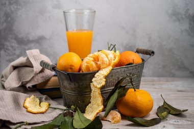 Konteynırda yaprakları olan birkaç mandalina beyaz bir masanın üzerinde, arka planda hafif bir zemine uzanır. Rustik biçim kopyalama uzayı.