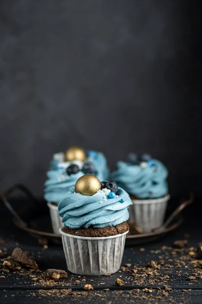 Vários muffins ou cupcakes com creme em forma de azul e blueberrieson na mesa preta. Estilo rústico copyspace. — Fotografia de Stock