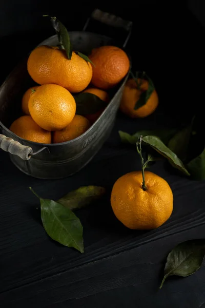 Varias mandarinas con hojas en un recipiente yacen sobre una mesa negra sobre un fondo oscuro. Copyspace estilo rústico. Imagen de stock