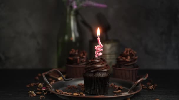 Mehrere Muffins oder Cupcakes mit Schokoladencreme am schwarzen Tisch. Festliche Kerzen brennen auf einem Schokoladenkuchen. 4k. Niemand. — Stockvideo