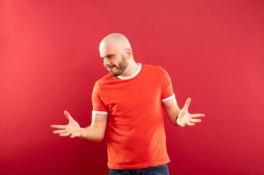 Kırmızı arka planda kırmızı tişörtlü, sakallı orta yaşlı bir adam neşeyle sağ tarafı gösteriyor. İzole edilmiş.