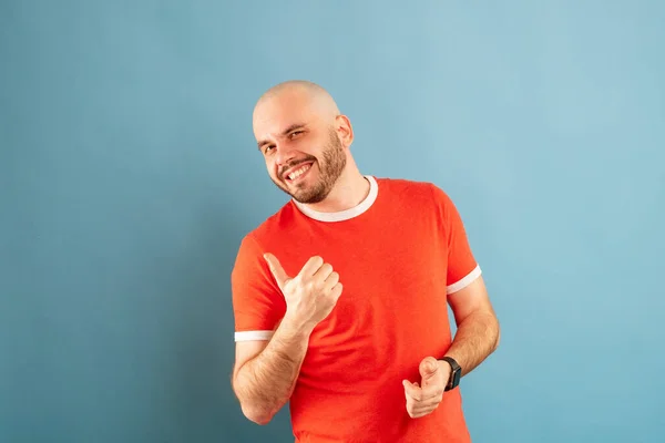 Ein Mann mittleren Alters mit Bart steht in einem roten T-Shirt vor blauem Hintergrund mit ausgestreckten Armen und jubelt über den Sieg. Isoliert. — Stockfoto