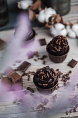 Beyaz masada çikolata şekilli kremalı birkaç kek ya da kek. Kutlama mumu çikolatalı pastada yanar. Yakınlarda çikolata parçaları var..