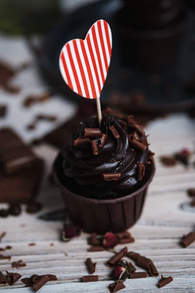Vários muffins ou cupcakes com creme em forma de chocolate na mesa branca. Um cartão de férias na forma de um coração do Dia de São Valentim em um deles. — Fotografia de Stock