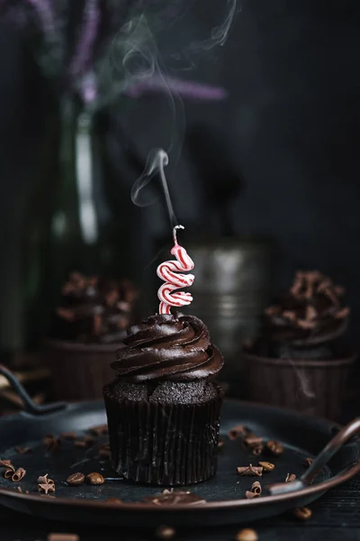 Vários muffins ou cupcakes com creme em forma de chocolate na mesa preta. Queimaduras de vela festivas em um bolo de chocolate — Fotografia de Stock