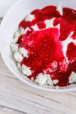 Beyaz ahşap bir masada beyaz bir kasede ekşi krema ve ahududu reçeli süzme peynir. Sağlıklı kahvaltı. Kırsal biçim