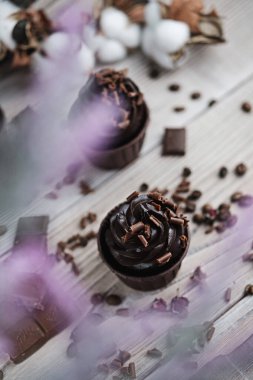 Beyaz masada çikolata şekilli kremalı birkaç kek ya da kek. Kutlama mumu çikolatalı pastada yanar. Dağınık çikolata parçaları var.