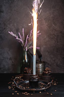 Birkaç kek ya da siyah masada çikolata şekilli kremalı kekler. Kutlama mumu çikolatalı pastada yanıyor.
