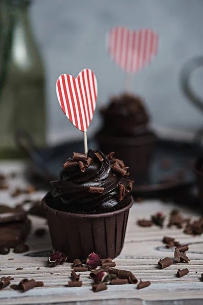 Vários muffins ou cupcakes com creme em forma de chocolate na mesa branca. Um cartão de férias na forma de um coração do Dia de São Valentim em um deles. — Fotografia de Stock