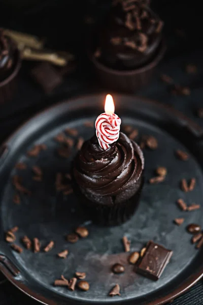 Vários muffins ou cupcakes com creme em forma de chocolate na mesa preta. Queimaduras de vela festivas em um bolo de chocolate — Fotografia de Stock