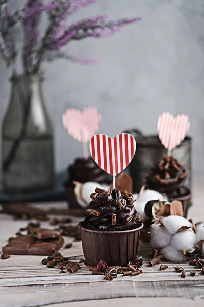 Varios panecillos o cupcakes con crema en forma de chocolate en la mesa blanca. La tarjeta de fiesta en forma del corazón para el Día de San Valentín en un de ellos. Fotos de stock