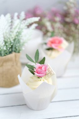 Beyaz tereyağı kremalı birkaç kek ve beyaz ahşap bir masada pembe bir gül. Sevgililer Günü ya da Anneler Günü hediyesi. Kırsal biçim.