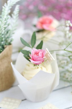 Beyaz tereyağı kremalı birkaç kek ve beyaz ahşap bir masada pembe bir gül. Sevgililer Günü ya da Anneler Günü hediyesi. Kırsal biçim.