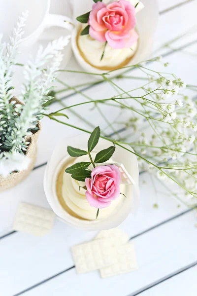 Beyaz tereyağı kremalı birkaç kek ve beyaz ahşap bir masada pembe bir gül. Sevgililer Günü ya da Anneler Günü hediyesi. Kırsal biçim.