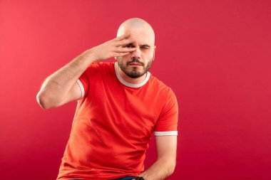 Kırmızı arka planda kırmızı tişörtlü, orta yaşlı sakallı bir adam zaferi eliyle gösteriyor. İzole edilmiş.