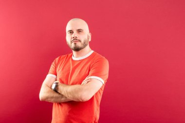 Kırmızı arka planda kırmızı tişörtlü, sakallı orta yaşlı bir adam neşeyle sağ tarafı gösteriyor. İzole edilmiş.